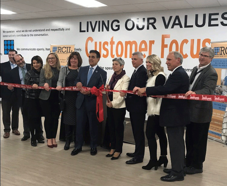 RCIL CEO, Board Members, Chamber Members and Local Dignitaries Standing with Ribbon in front of a wall that reads Living our Values - Customer Focus